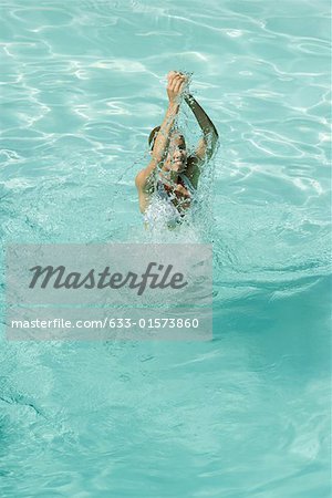 Young woman standing in pool, splashing with arms over head, full length, high angle view