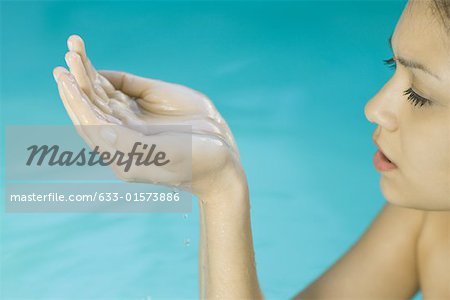 Young woman in water, holding up cupped hands, cropped view