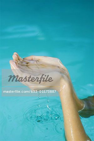 Young woman holding up cupped hands full of water, cropped view