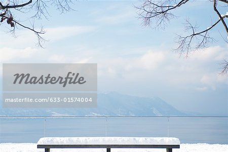 Snow-covered bench overlooking lake and mountains
