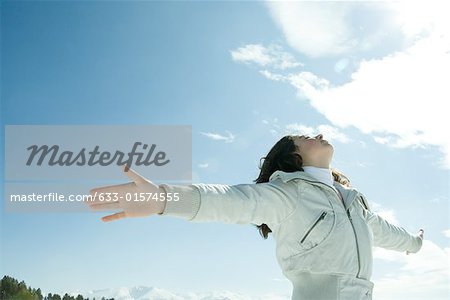 Teen girl standing in snowy landscape, arms raised to sun