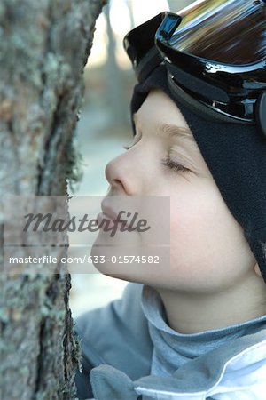 Boy leaning face close to tree, eyes closed