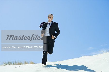 Man in suit and tie running across dune, laughing