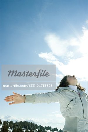 Teen girl standing in snowy landscape with head back and arms out, low angle view