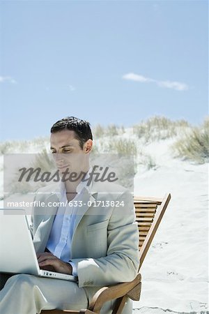 Businessman sitting in deck chair at beach, using laZSop