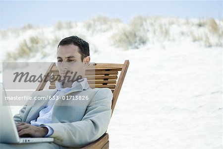 Businessman sitting in deck chair at beach, using laZSop