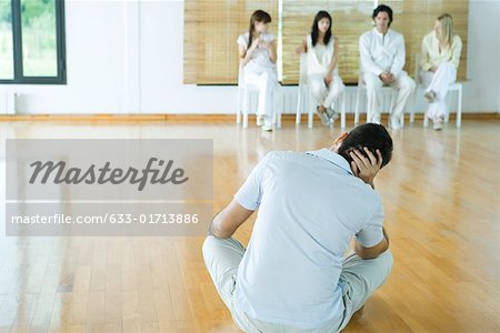 Man sitting on floor, facing group sitting in chairs