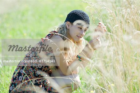 Young woman crouching in field, touching tall grass