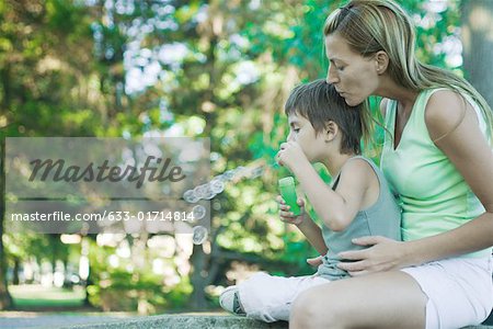 Boy and mother blowing bubbles, side view