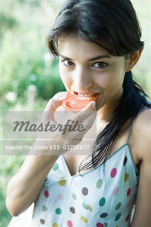 Young woman taking bite out of tomato half