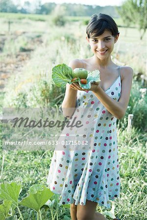 Young woman holding up fresh produce in cabbage leaves, smiling at camera