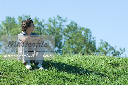 Teen boy sitting on grassy hill, relaxing