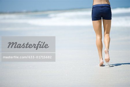 Young woman running on beach, waist down, rear view