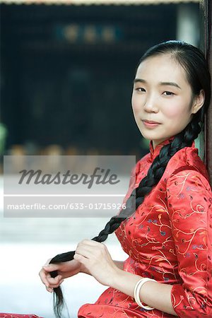 Young woman dressed in traditional Chinese clothing, holding her long braided hair, looking at camera