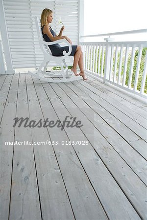 Woman sitting in rocking chair on porch, holding flower, side view