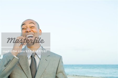 Businessman using cell phone at the beach, smiling, eyes closed