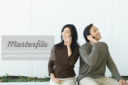 Couple sitting side by side, both using cell phones