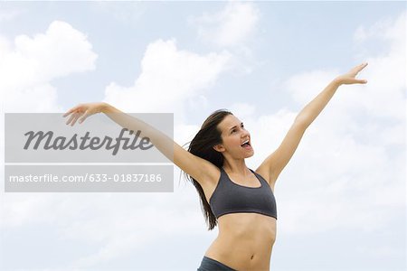 Young woman outdoors with arms raised, open mouth, looking away