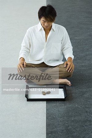 Man sitting on floor, looking down at rock garden