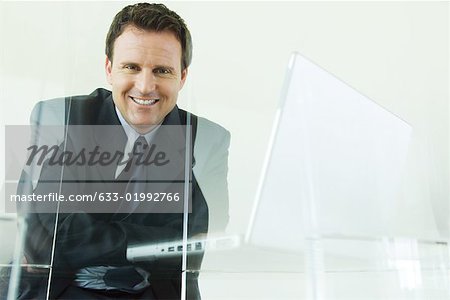 Businessman sitting next to laZSop computer, smiling at camera