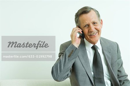 Businessman using cell phone, smiling at camera