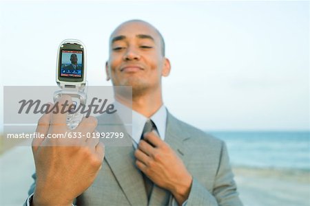 Businessman photographing self with cell phone at the beach, smiling, adjusting tie