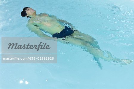 Man floating on back in swimming pool, eyes closed