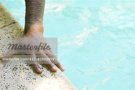 Man's hand holding side of swimming pool, close-up, cropped