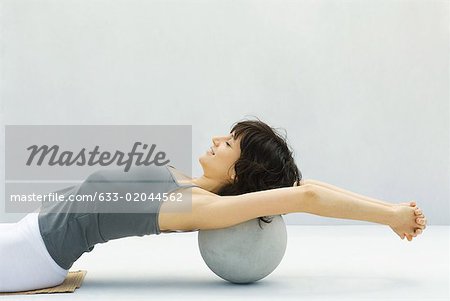 Woman leaning back against fitness ball, arms outstretched, side view