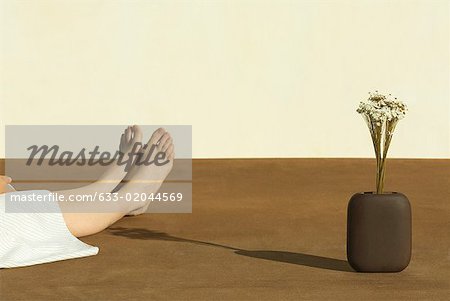 Woman sitting on the ground next to flowers in vase, cropped view