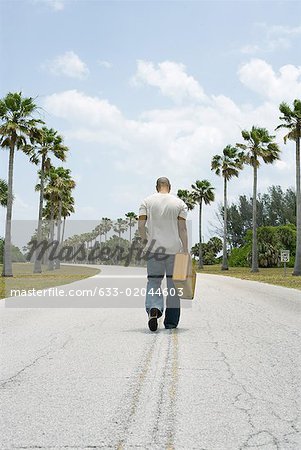 Man walking in center of road, carrying suitcase, rear view