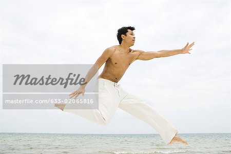 Man leaping in the air, side view, ocean in background