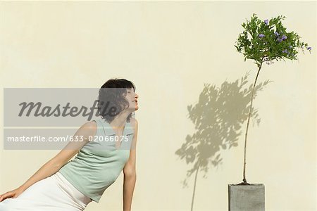 Woman sitting outdoors, leaning toward flowering plant, eyes closed