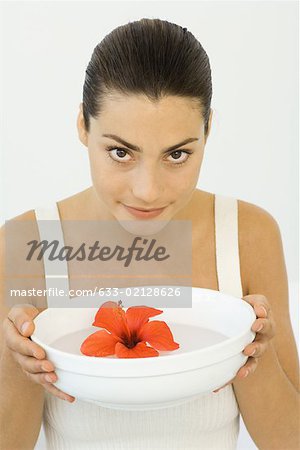 Woman holding hibiscus blossom in bowl of water, smiling at camera