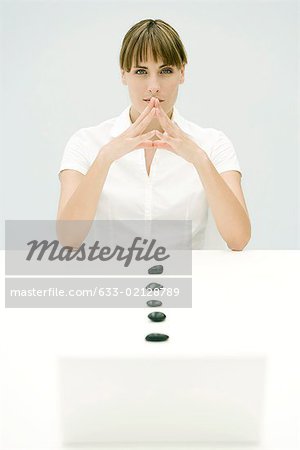 Woman sitting with stones, hands clasped, looking at camera