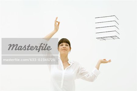 Woman raising arms, eyes closed, cube floating in midair