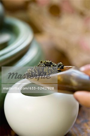 Tea scoop pouring loose tea leaves into teapot