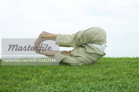 Senior woman lying on back and touching toes outdoors