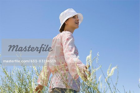 Young woman walking through field of tall grass with arms out, smiling