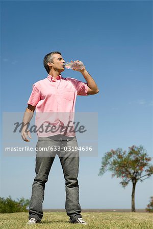 Man drinking water from a bottle at a gym - Stock Photo - Masterfile