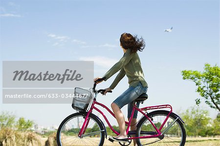 Woman riding bicycle, looking at plane flying in sky