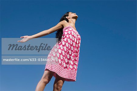 Woman standing outdoors with arms out and eyes closed, low angle view