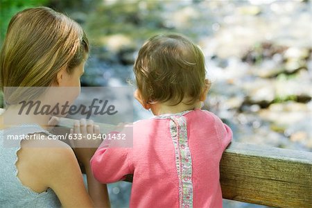 Girl and baby sister looking over railing, rear view