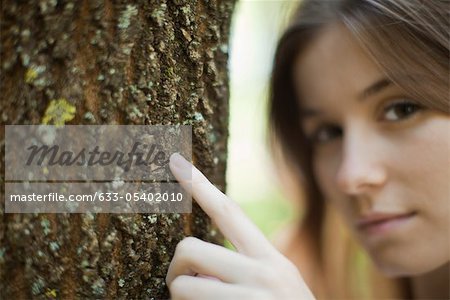 Young woman's finger touching tree trunk, cropped
