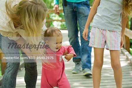 Baby girl learning to walk outdoors with family
