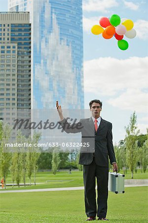 Businessman releasing bunch of balloons into air, looking disappointed
