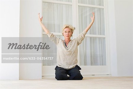 Mature woman sitting on heels with arms raised