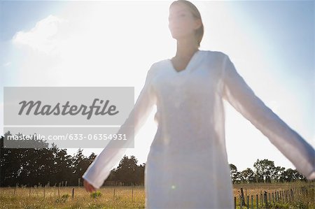 Mid-adult woman standing in field with eyes closed and arms outstretched