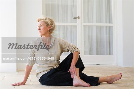Mature woman sitting on floor doing spinal twist
