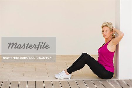 Mature woman sitting against wall with arms behind back